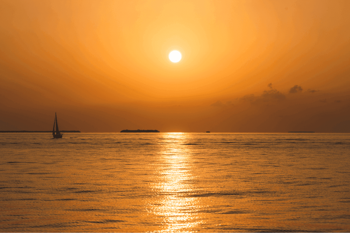 Sunset over Key West ocean with sailboat, perfect for Key West boat rentals and island adventures.