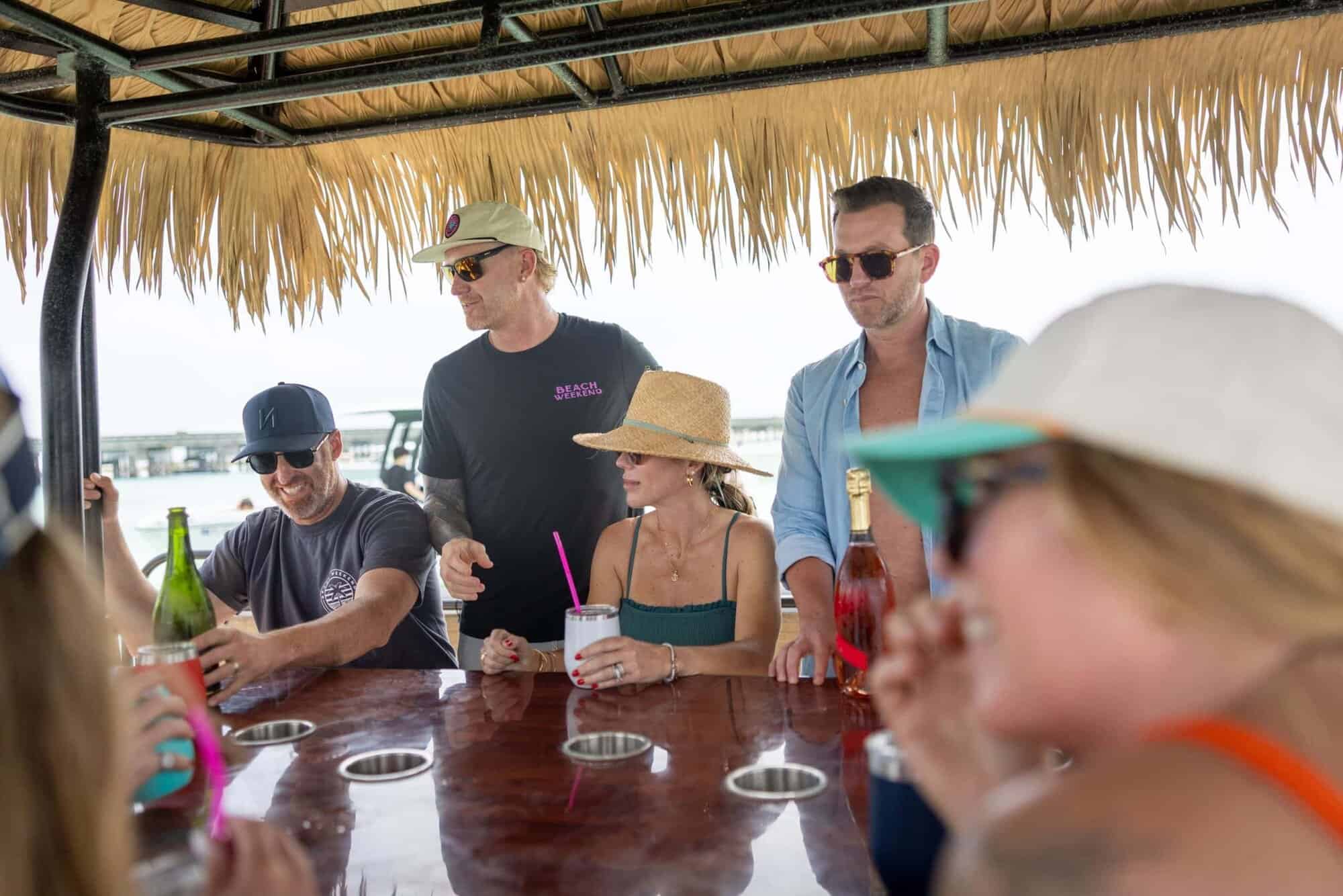 Relaxing group of friends enjoying drinks at Key West boat rentals under a tiki hut canopy with ocean view in the background, perfect for a fun day on the water in Key West.