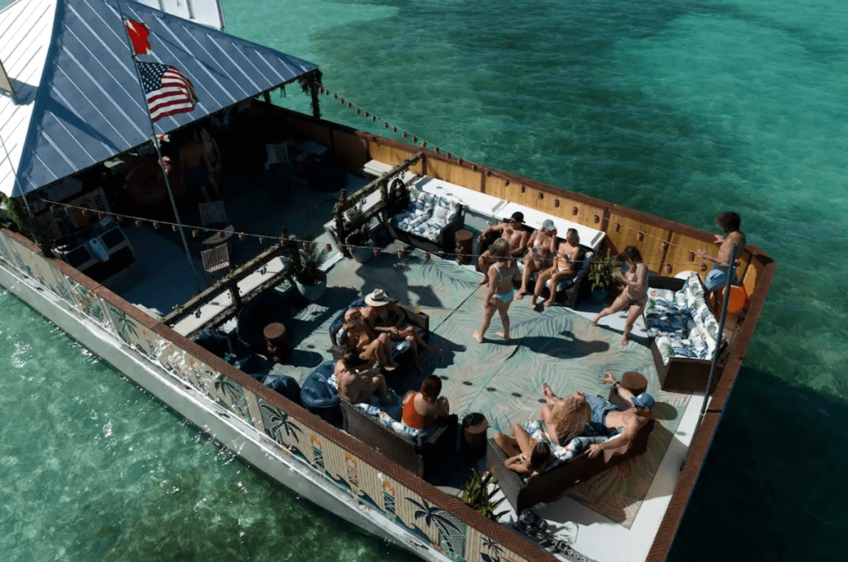 Aerial view of a lively Key West boat rental with people relaxing and socializing on the deck, enjoying the sun and tropical atmosphere in crystal-clear waters.